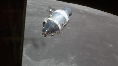 Das Apollo-15-Raumschiff im Mondorbit vor der grauen Mondoberflaeche, an der Flanke des Servicemoduls sind zwei kreuzfoermige Triebwerksgruppen zu erkennen