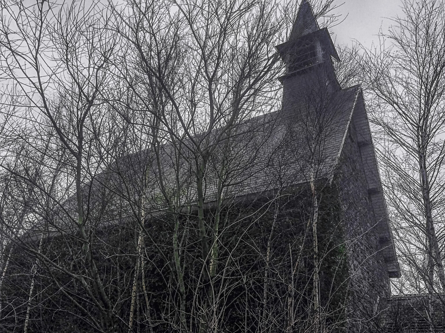 Verlassene Klosterkapelle mit Dachreiter zwischen kahlen Bäumen unter trübem Himmel im Lost Place