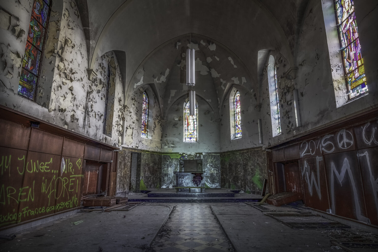 Kapellenchor mit Buntglasfenstern und stark abblätterndem Putz am Altar im Lost Place