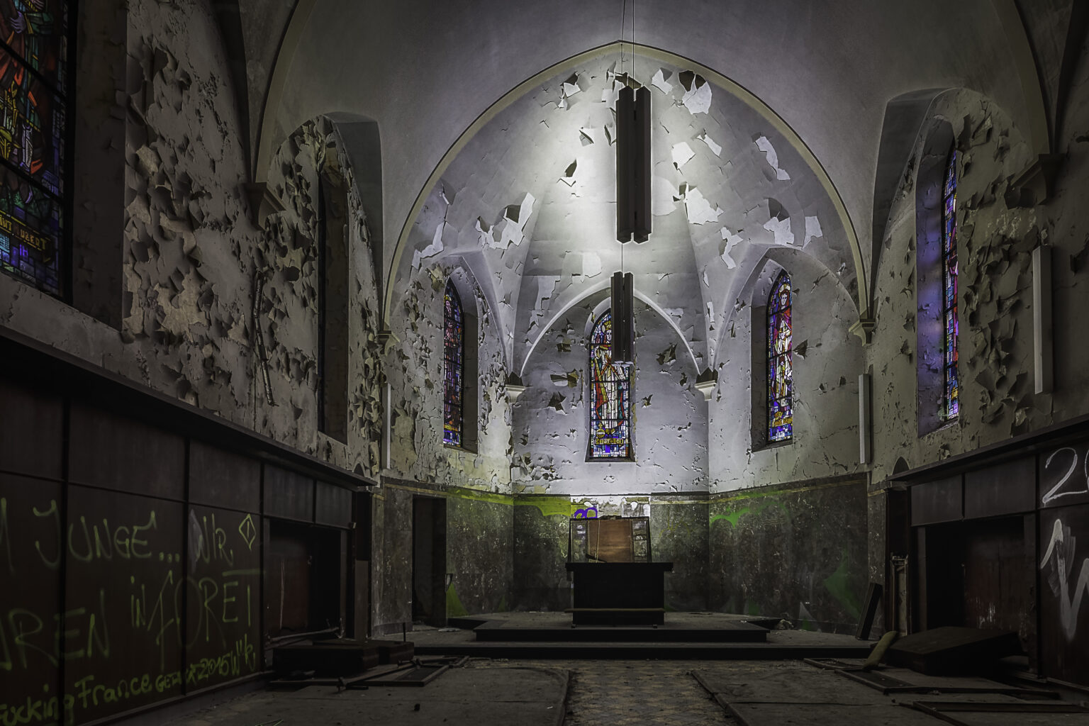Kapellenchor mit weißer Gewölbeapsis, abblätterndem Putz und Buntglas am Altar im Lost Place