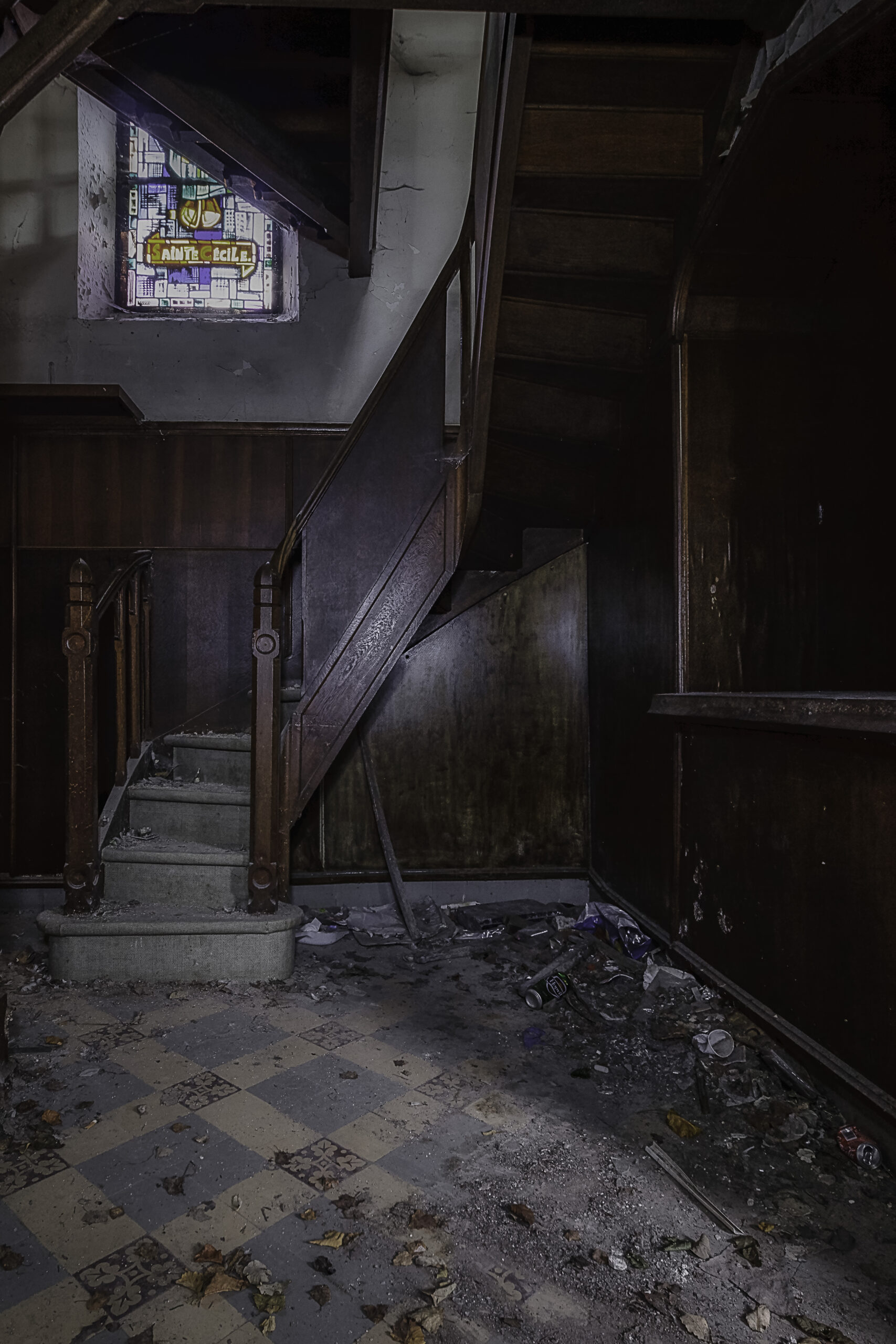 Holztreppe mit Buntglasfenster und Schachbrettboden im verlassenen Kloster