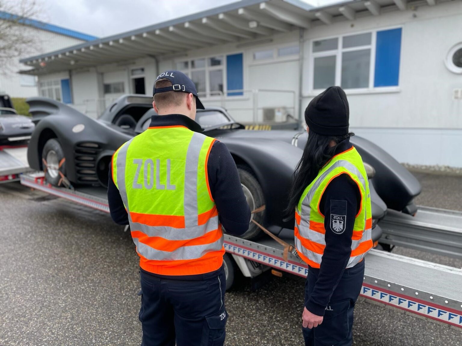 Zwei Zollbeamte vor einem schwarzen Batmobil-Replika auf einem Autotransporter