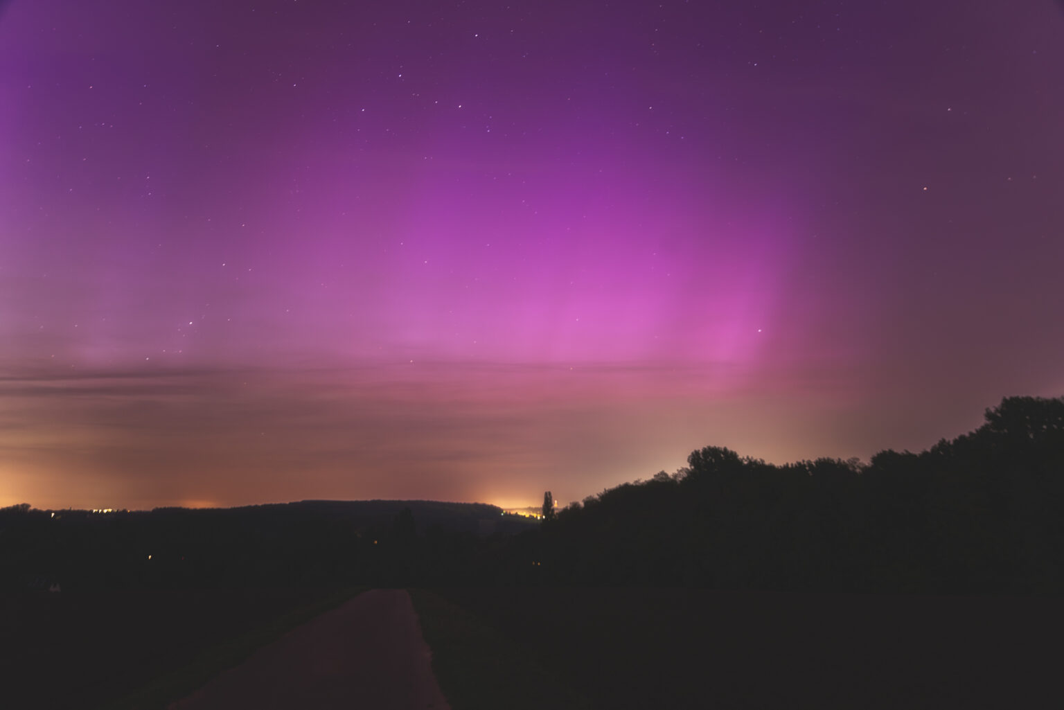 Pink-violettes Polarlicht über hügeliger Landschaft in NRW