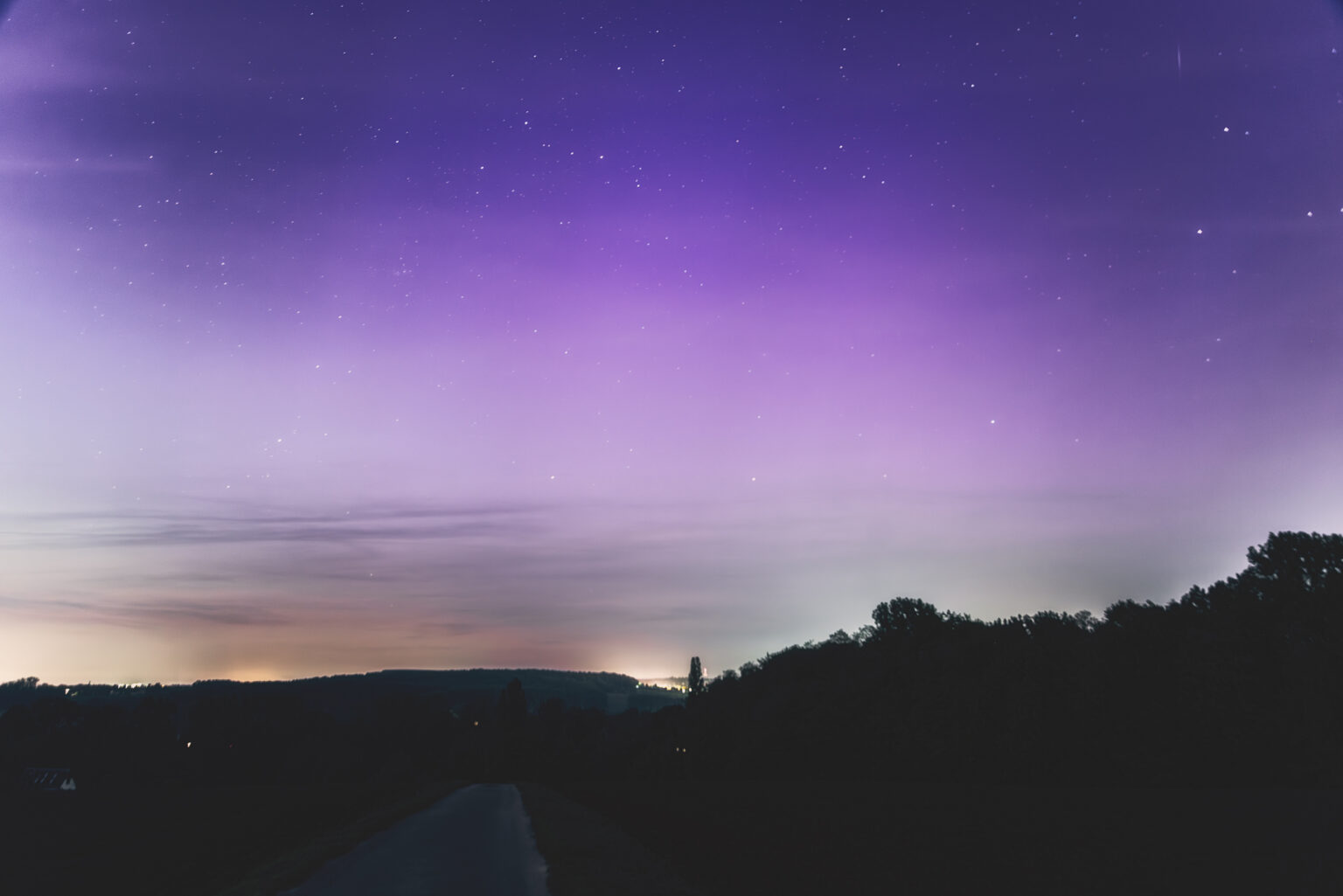 Violettes Polarlicht mit Sternenhimmel über Feldweg in NRW