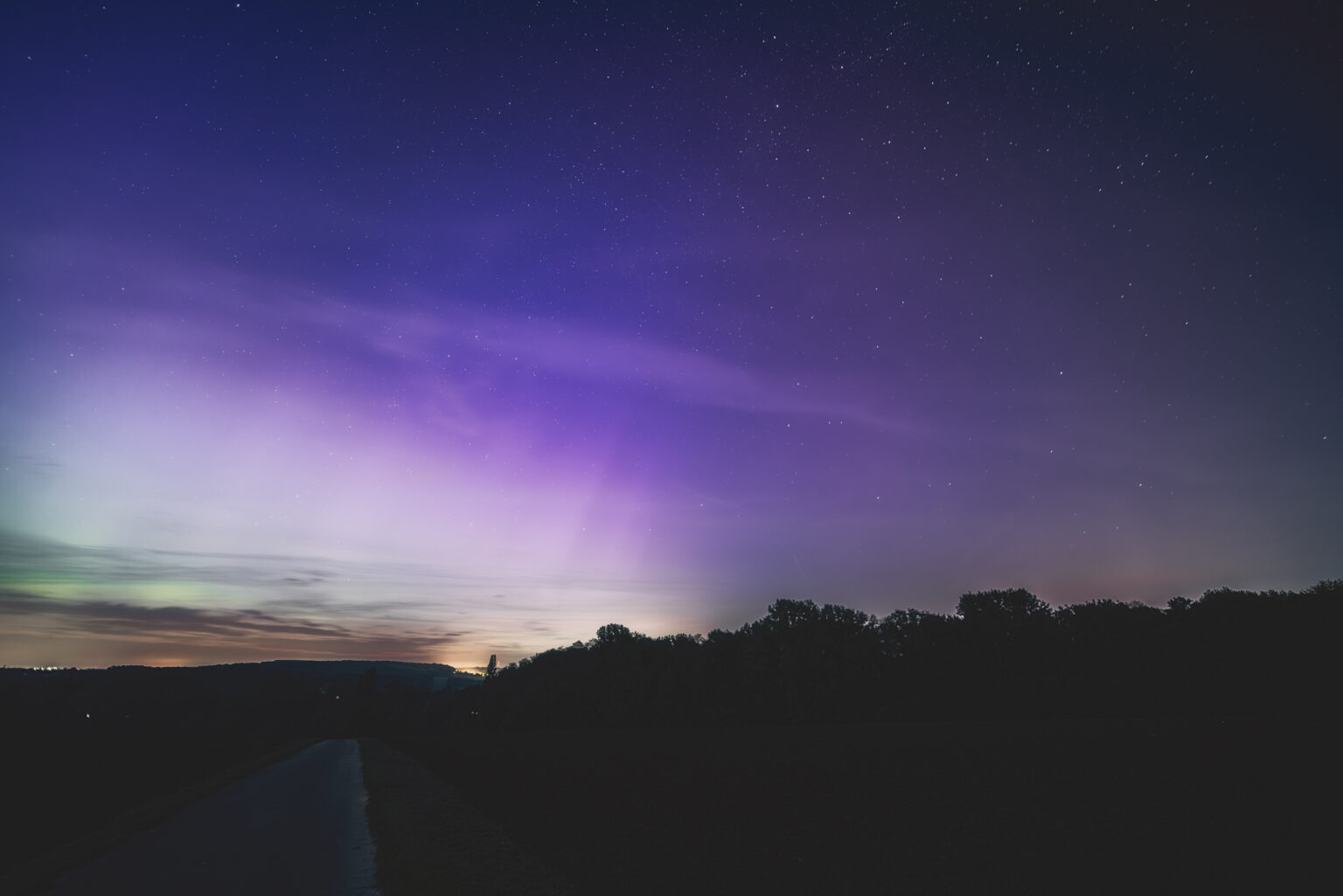 Violettes Polarlicht mit Strahlen über bewaldeter Hügelkante in NRW