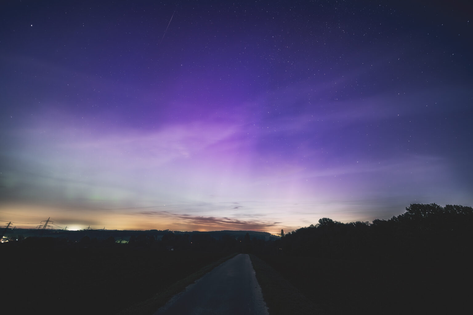 Weites violettes Polarlicht über Feldlandschaft mit Strommasten in NRW