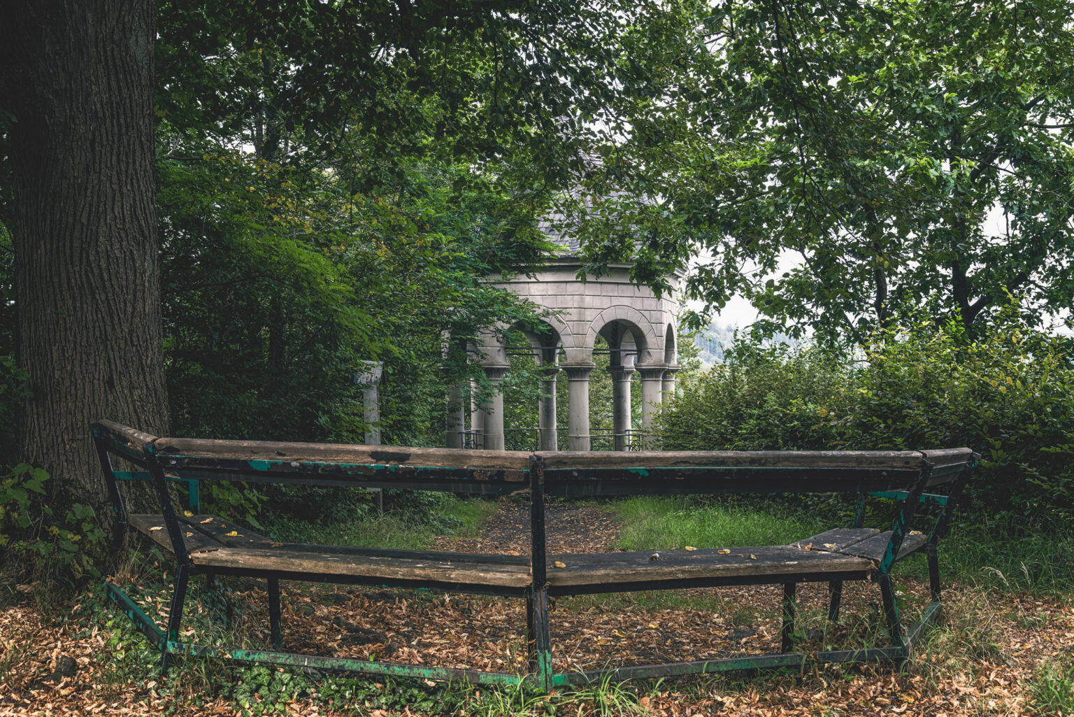 Klassizistischer Säulenpavillon im Wald mit alter geschwungener Holzbank im Bergischen Land