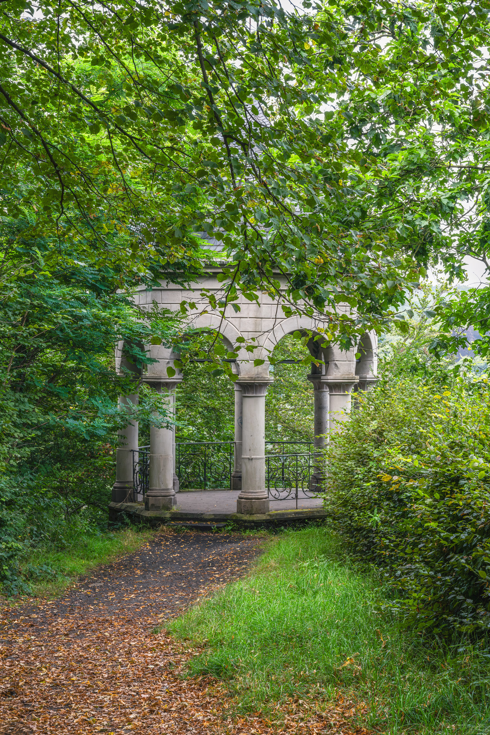 Klassizistischer Steinpavillon mit Bögen und Schmiedeeisengeländer am Waldweg im Bergischen Land
