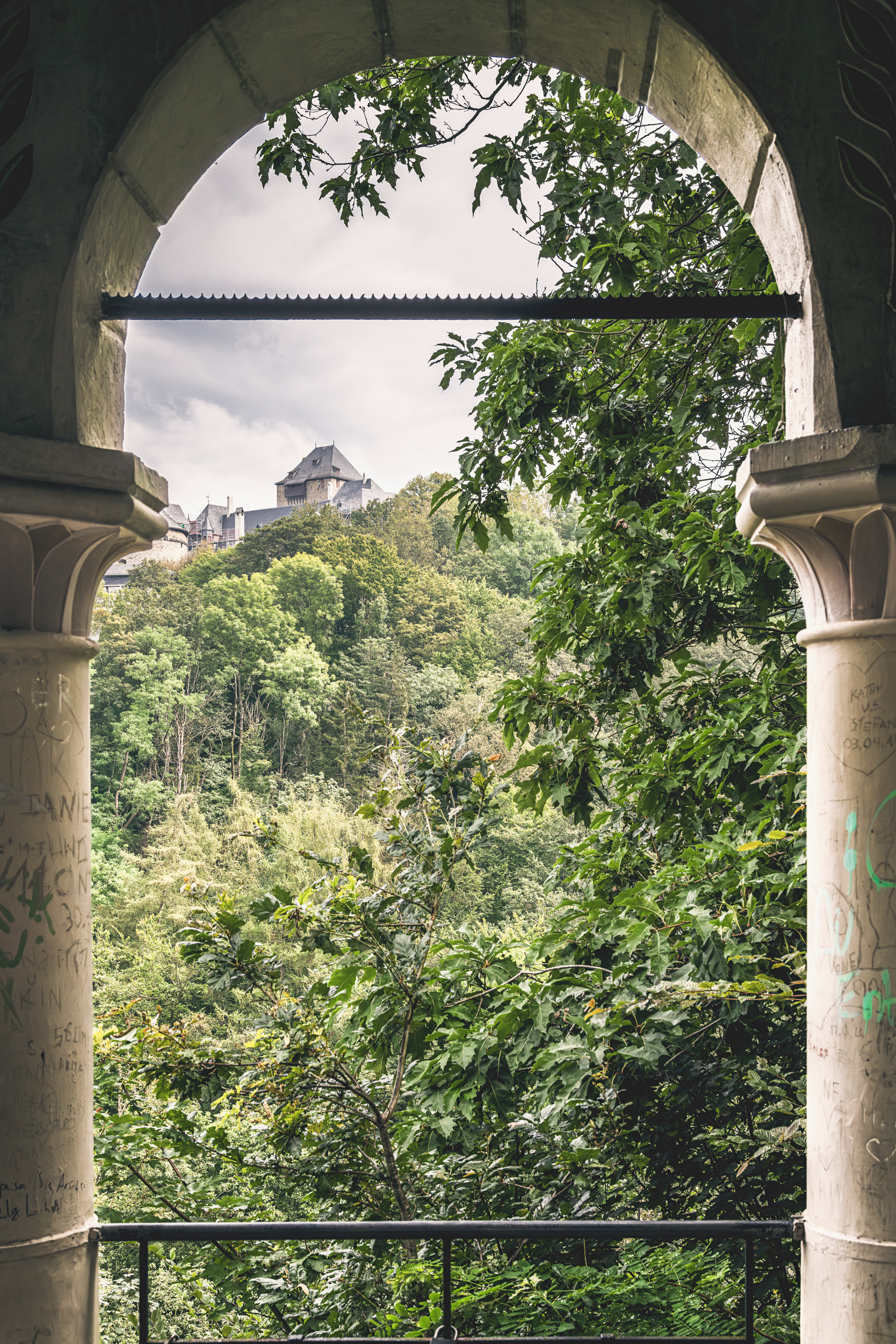 Blick durch einen Pavillonbogen auf ein Schloss auf bewaldetem Hügel im Bergischen Land