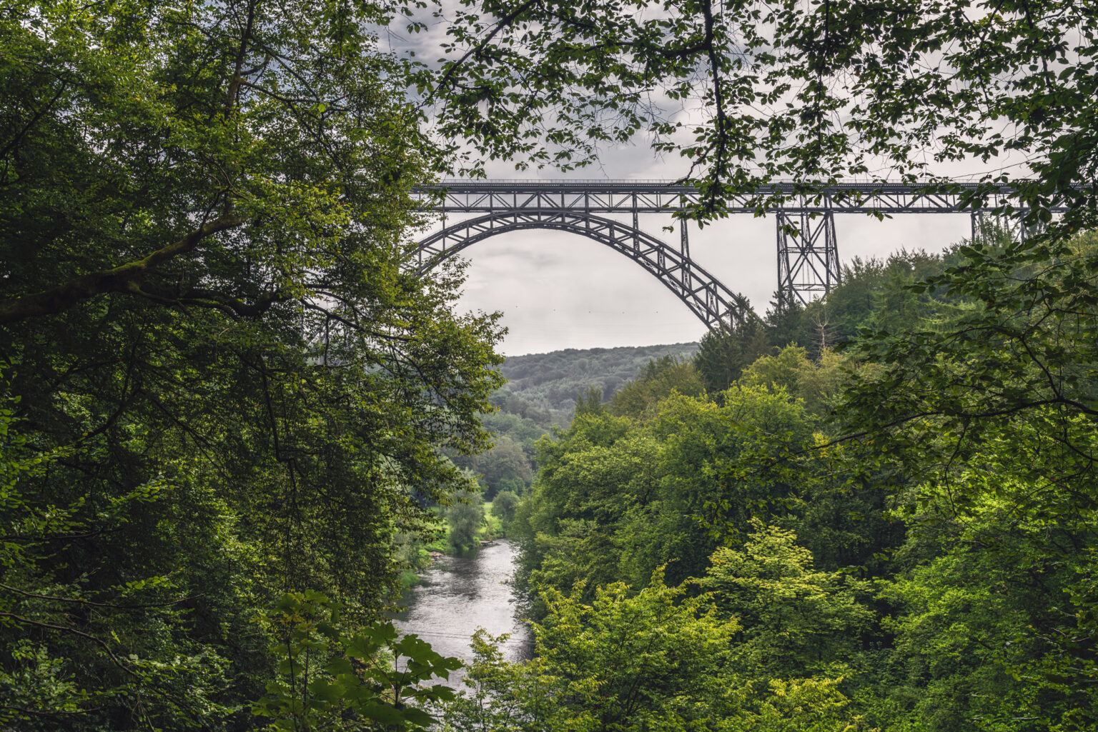 Stahlbogen der Müngstener Brücke über der Wupper, gerahmt von grünem Laub