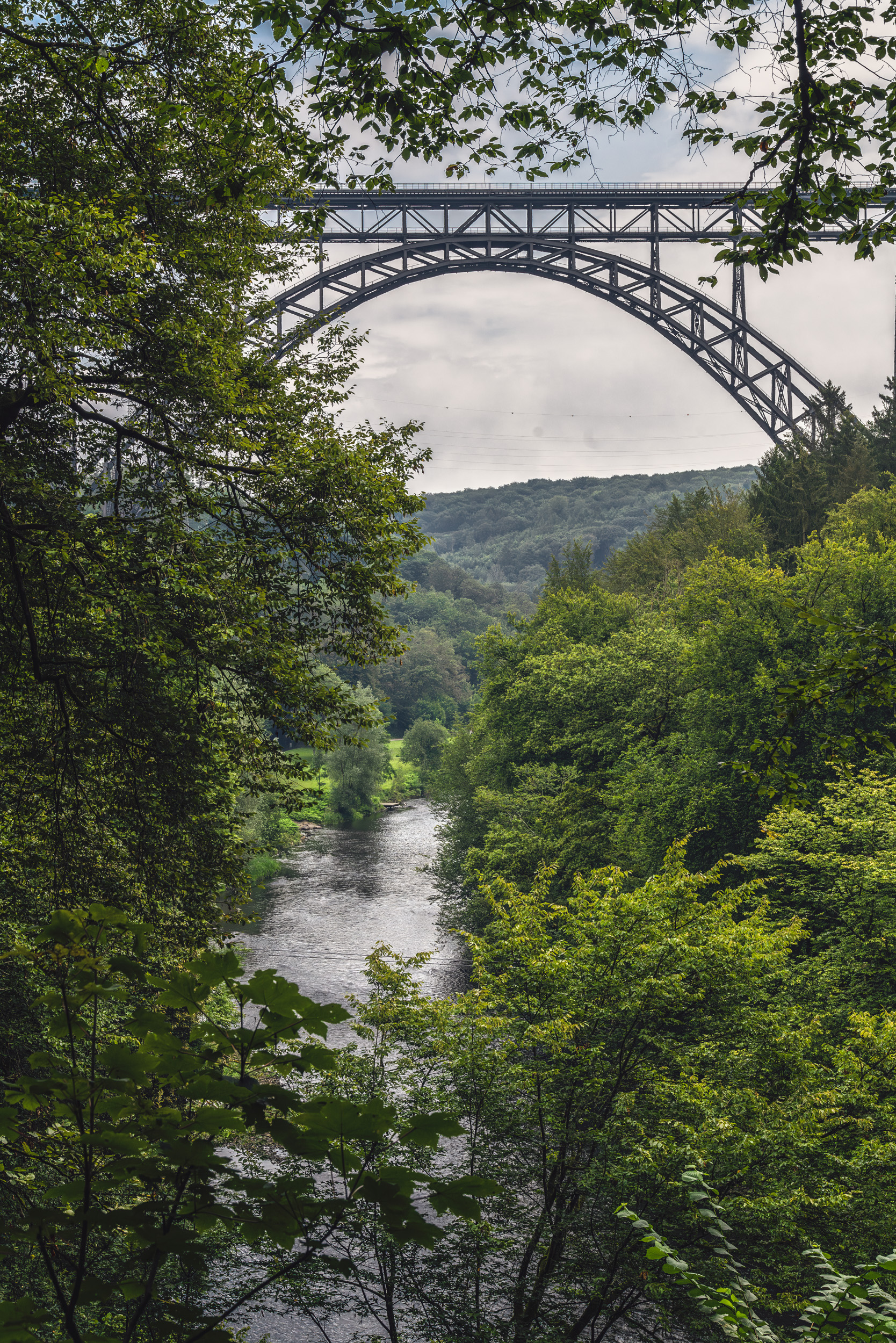 Hoher Stahlbogen der Müngstener Brücke über der Wupper im Hochformat durch Bäume