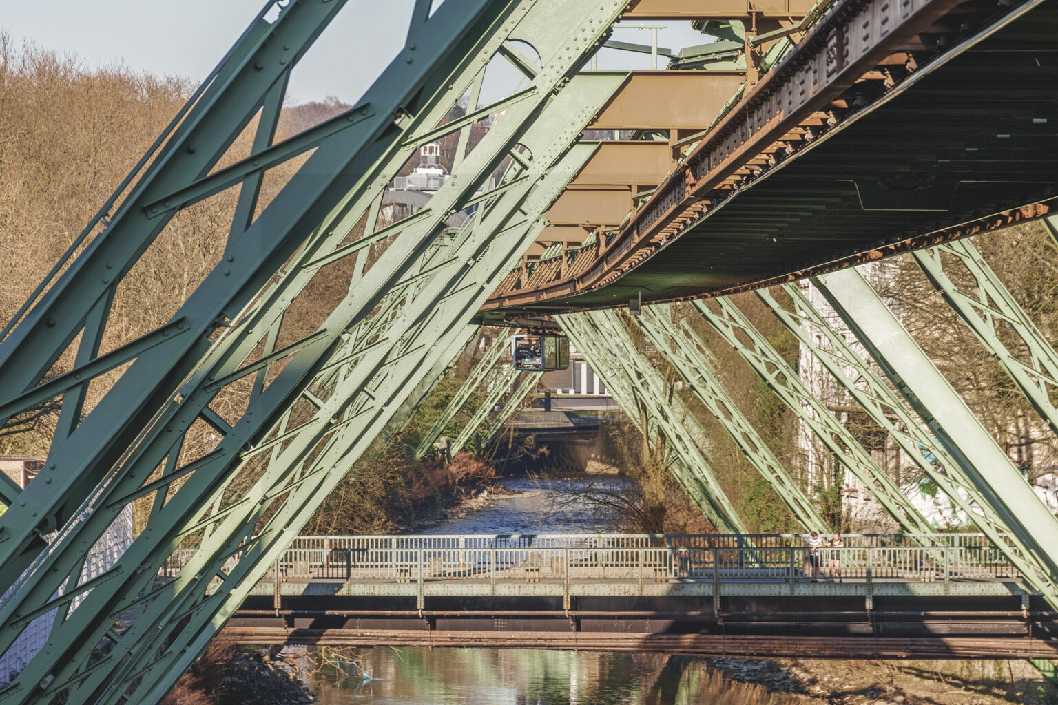 Grünes Stahlgerüst der Wuppertaler Schwebebahn über der Wupper und einer Brücke