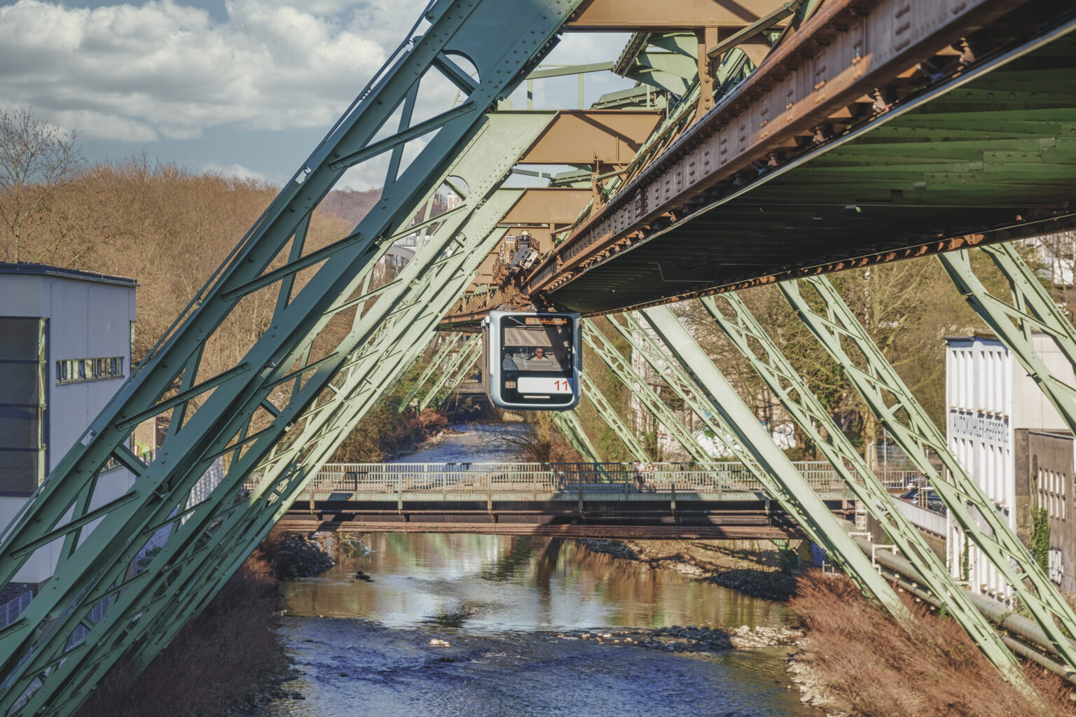 Schwebebahnwagen zwischen grünen Stahlträgern über der Wupper im Wintersonnenlicht
