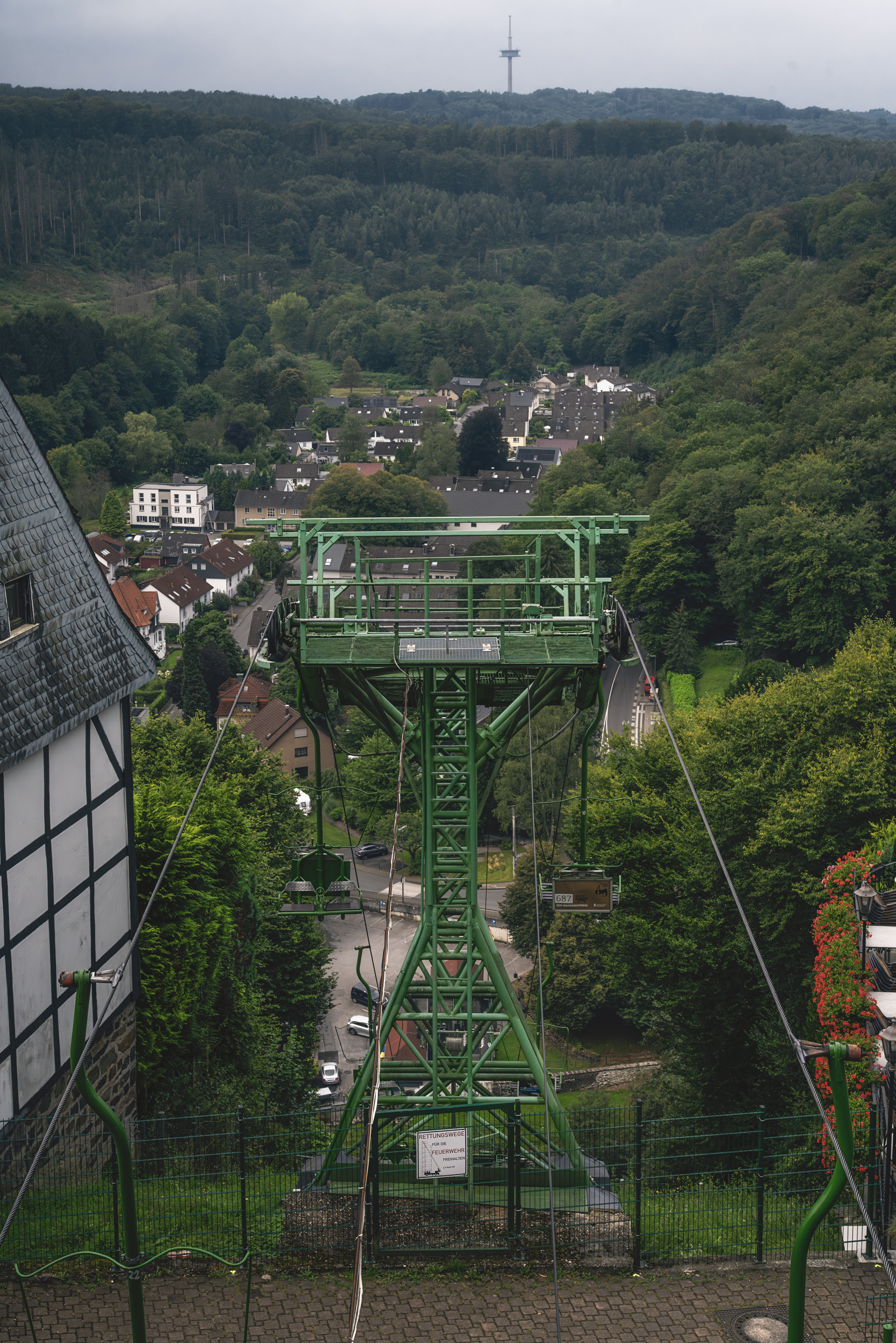 Grüne Sessellift-Stütze mit Seilen hinab zu einem Talort im Bergischen Land
