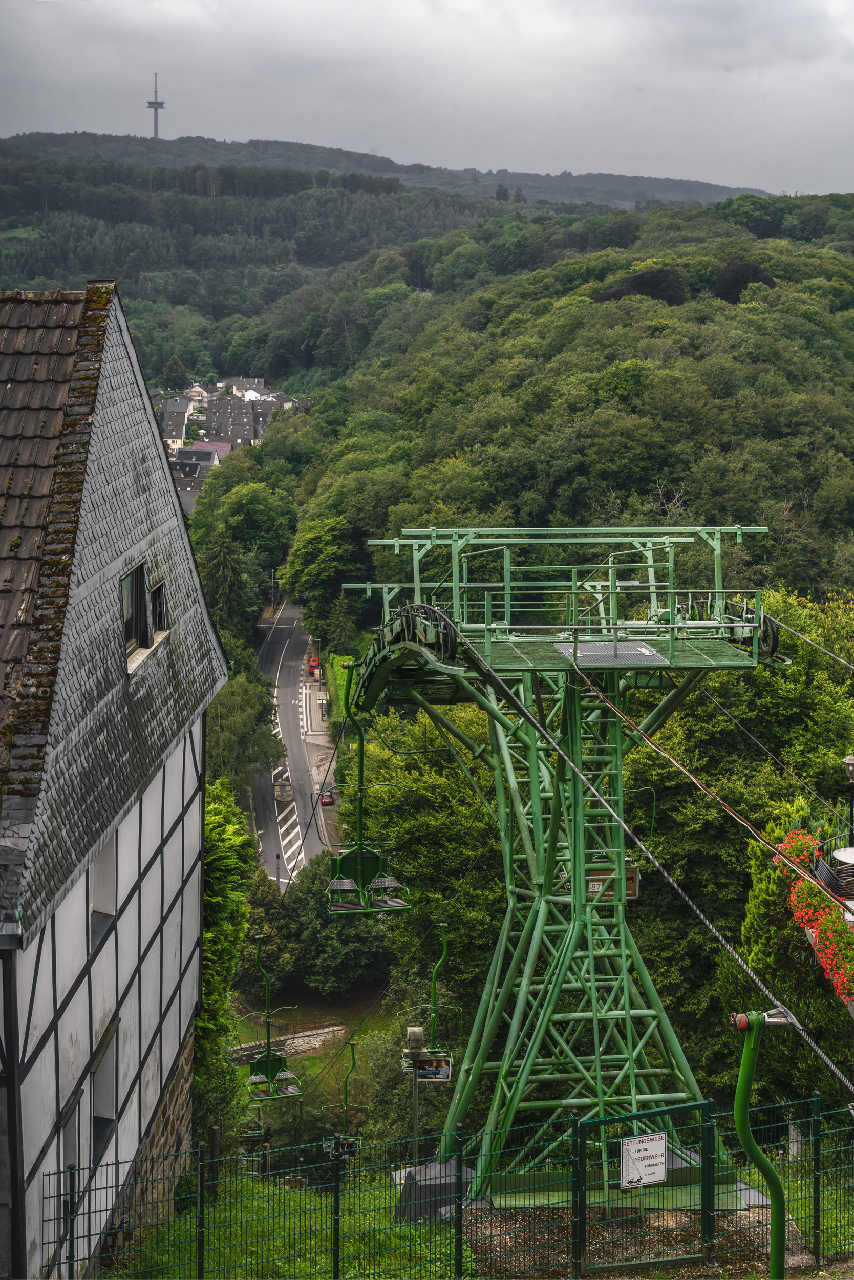 Grüne Sessellift-Stütze führt hinab in ein Bergisches Talstädtchen mit Fachwerkhaus