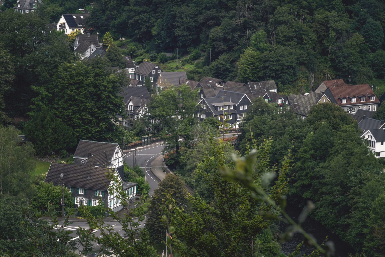 Bergisches Schiefer- und Fachwerkdorf in einem bewaldeten Tal mit kurviger Straße