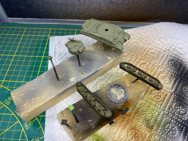 Olivgrün lackierte Turm- und Wannenteile zweier Panzermodelle auf Stützen mit Zwei-Euro-Münze als Größenvergleich