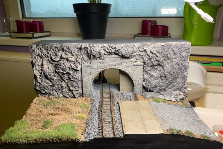 Tunnelportal-Diorama auf einer Fensterbank mit Pflanze und Kerzen im Hintergrund