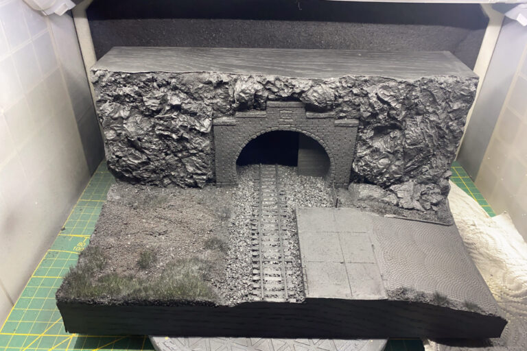 Grau grundiertes Tunnelportal-Diorama mit Felswand, Backsteinbogen und Gleis auf der Werkbank
