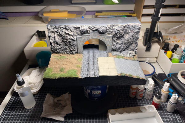 Tunnelportal-Diorama auf der Werkbank umgeben von Farben, Pinseln und Werkzeug