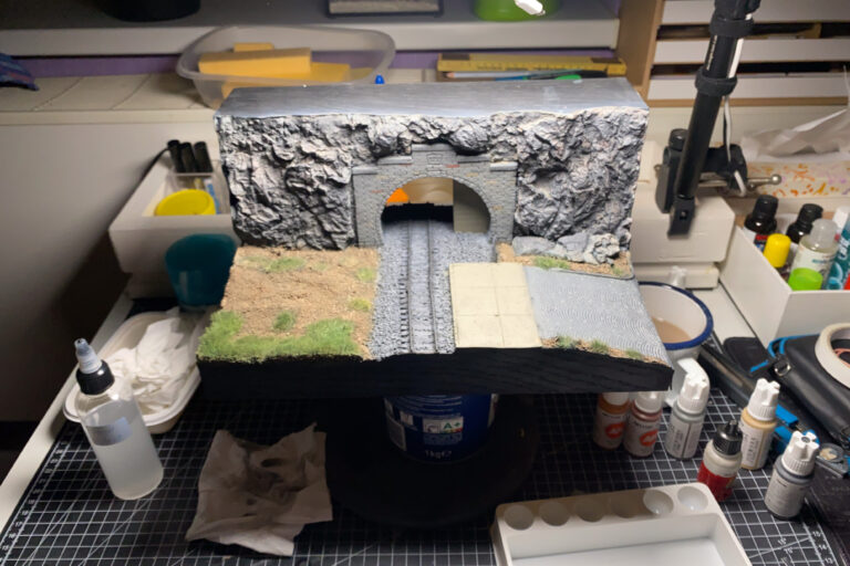 Tunnelportal-Diorama auf der Werkbank umgeben von Farben, Pinseln und Werkzeug