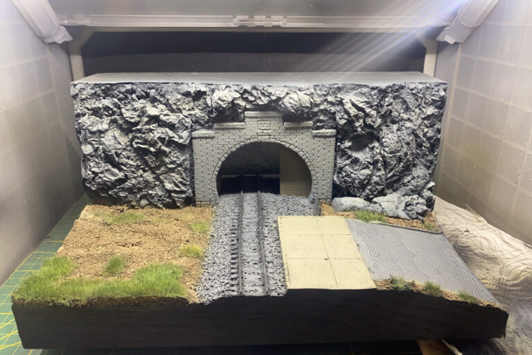 Hell ausgeleuchtetes Tunnelportal-Diorama mit grauer Felswand, Gleis und Grasböschung