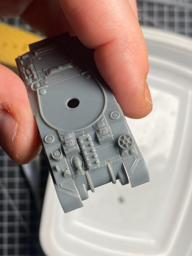 Grau grundiertes Wannenteil eines Sherman-Panzermodells in der Hand über einer Lackierwanne