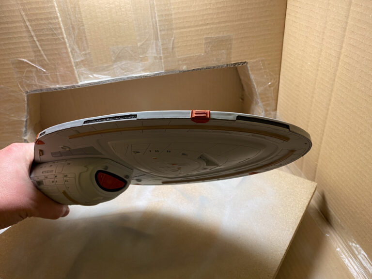 Untertassen-Unterseite der USS Voyager in der Hand mit blauem Deflektor über einem Karton