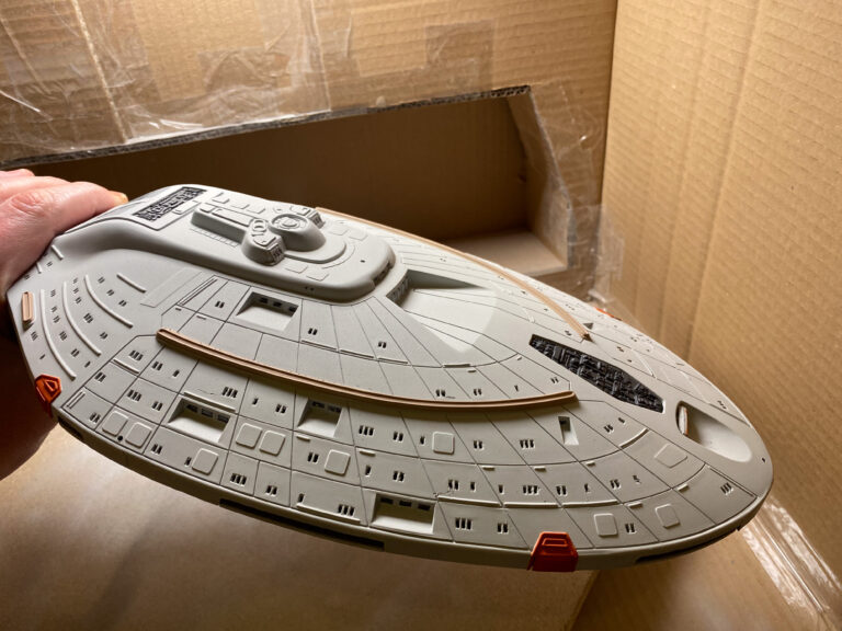 Grau lackierte Untertassen-Unterseite der USS Voyager in der Hand über einem Karton