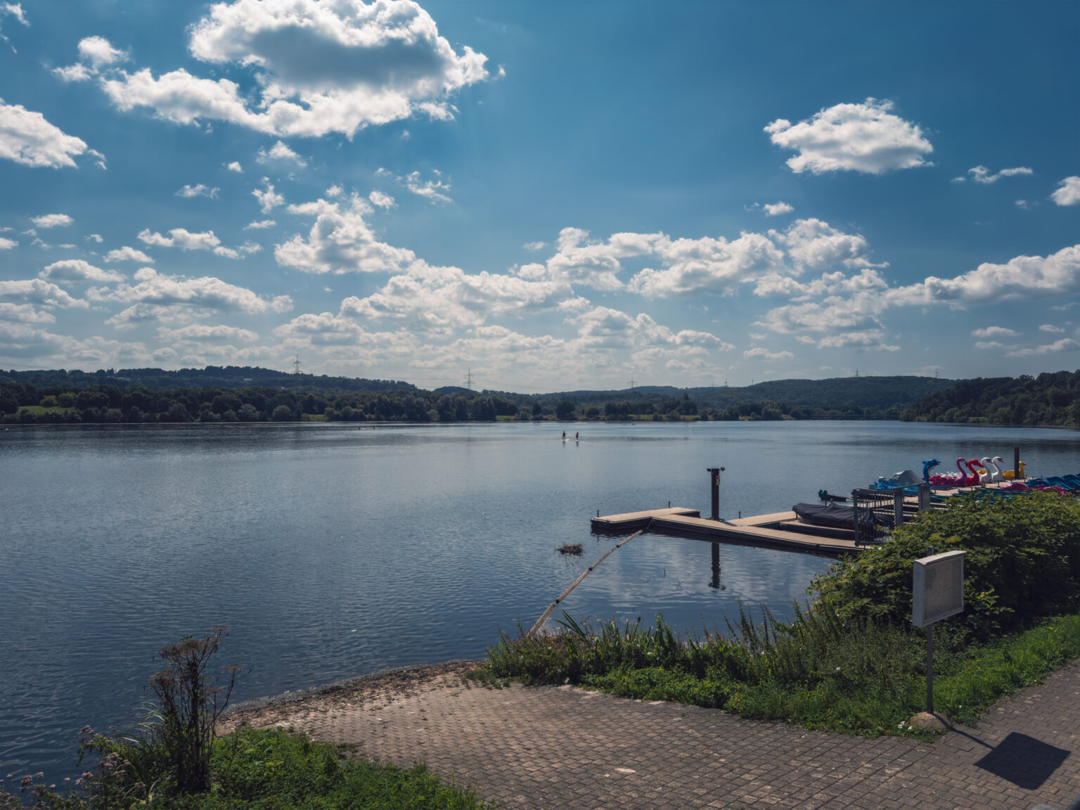 Weiter Stausee im Ruhrtal mit Bootssteg und Tretbooten unter Wolkenhimmel