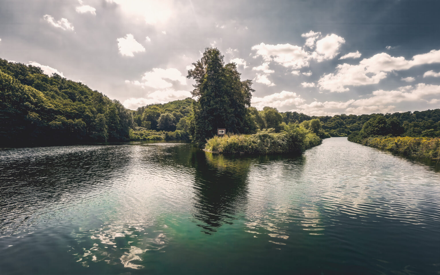 Flussinsel in der Ruhr unter dramatischem Wolkenhimmel mit bewaldeten Ufern