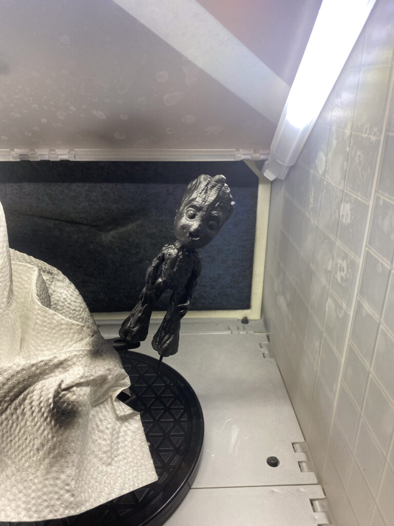 Schwarz grundierte Baby-Groot-Figur auf einem Drehteller in der Lackierbox