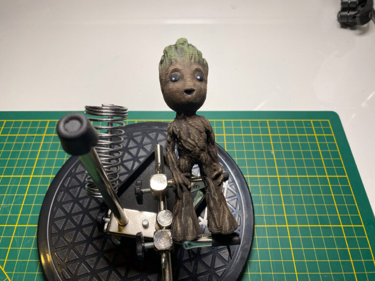 Fertig bemalte Baby-Groot-Figur in der Frontansicht auf einem Drehteller über der Schneidematte