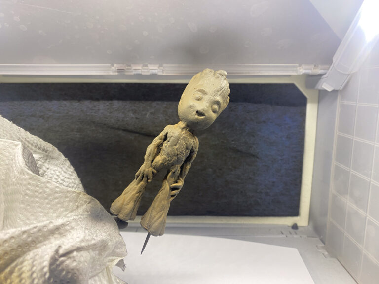 Roh geschliffene graue Baby-Groot-Figur auf einem Haltestift in der Lackierbox