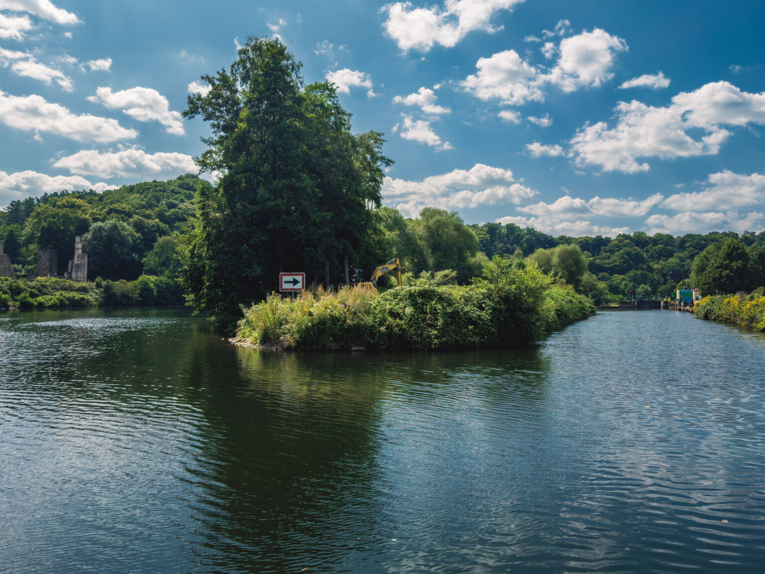 Bewachsene Flussinsel in der Ruhr mit einem Wegweiser unter sommerlichem Wolkenhimmel
