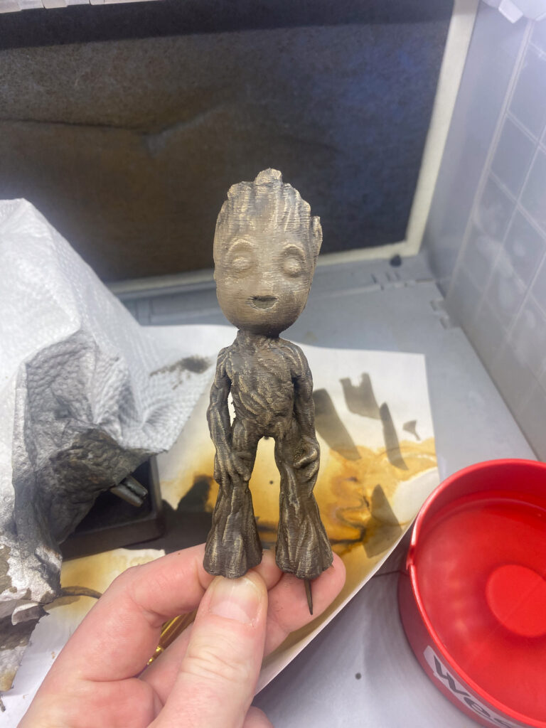 Grau trockengebürstete Baby-Groot-Figur mit betonter Rindenstruktur in der Hand