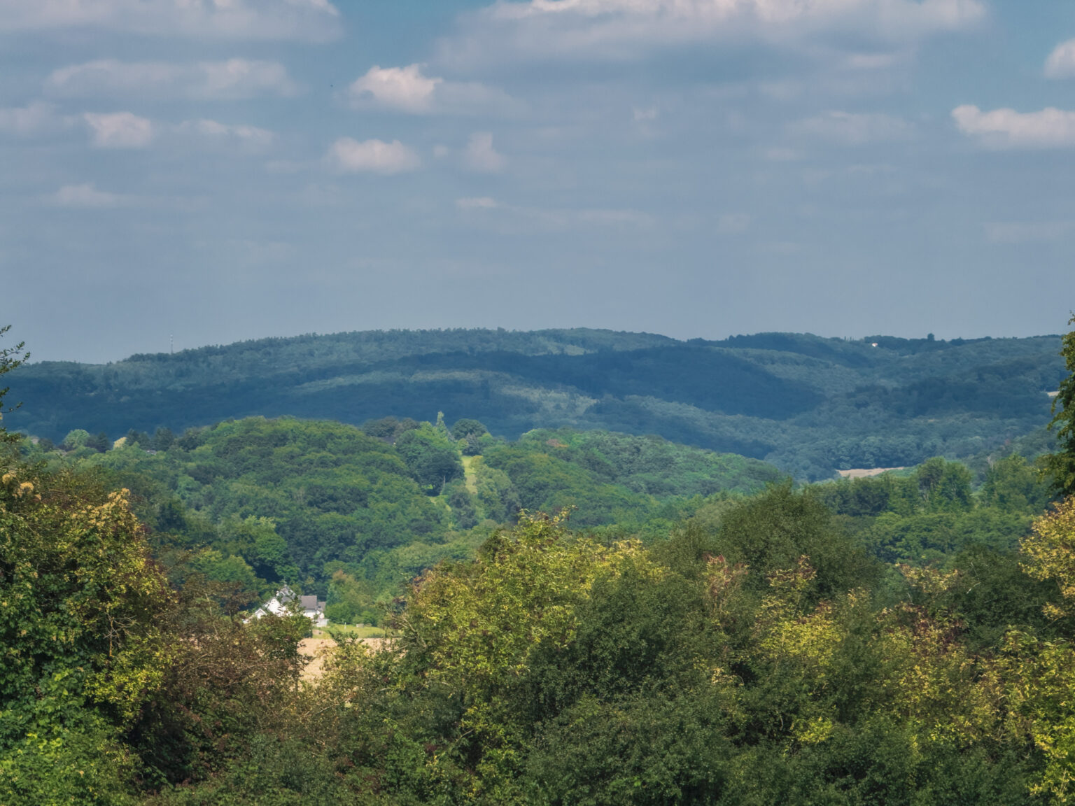 Panorama über bewaldete Höhenzüge im Bergischen Land unter diesigem Sommerhimmel