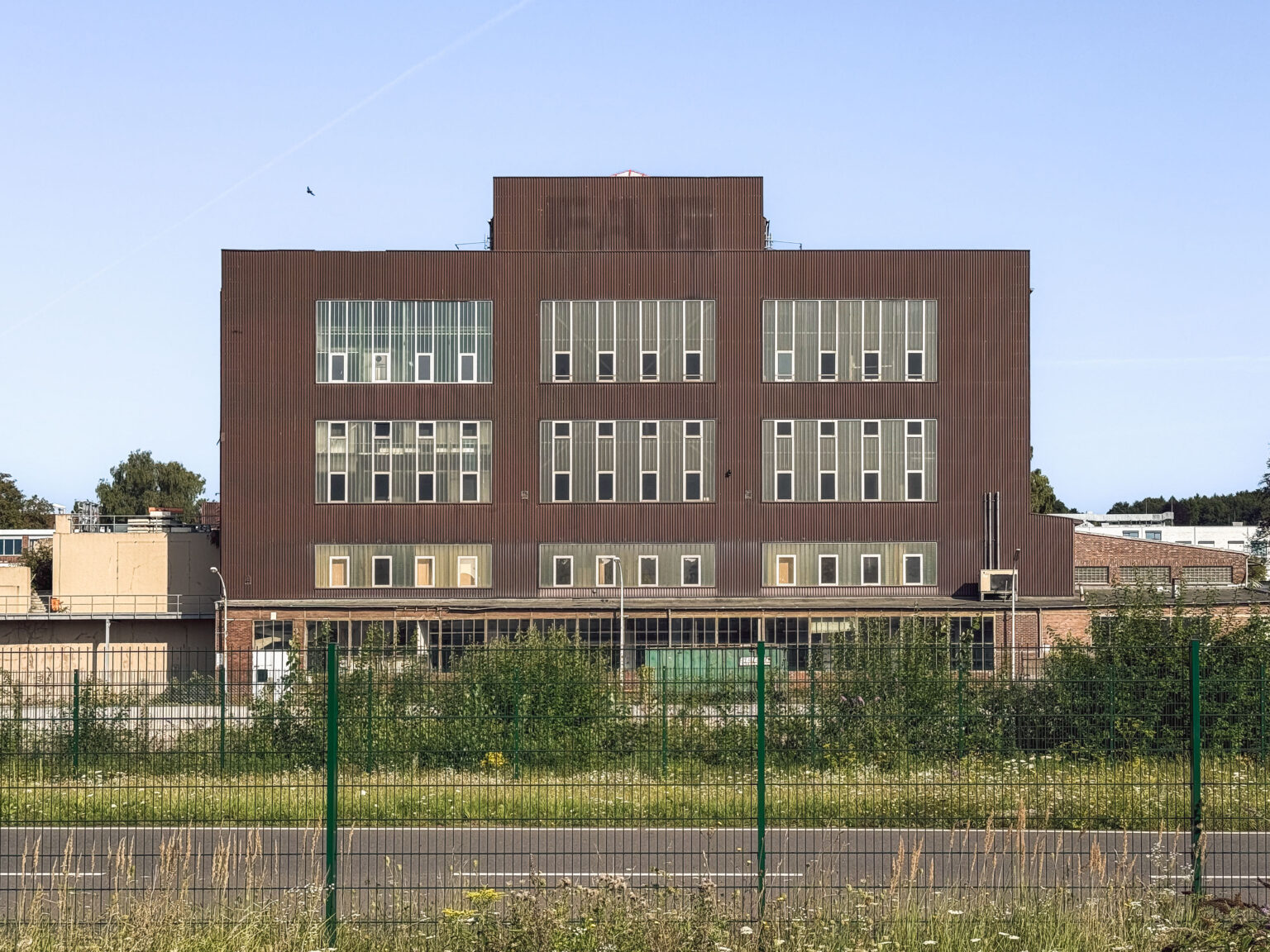 Großes braunes Industriegebäude hinter Zaun und Bahngleis im Revier