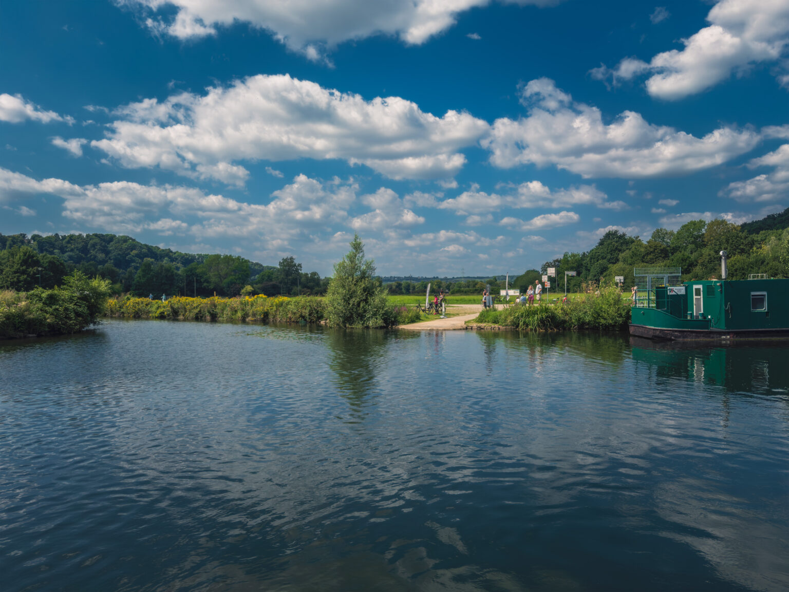 Flussbiegung der Ruhr mit grünem Hausboot und Menschen auf dem Uferweg