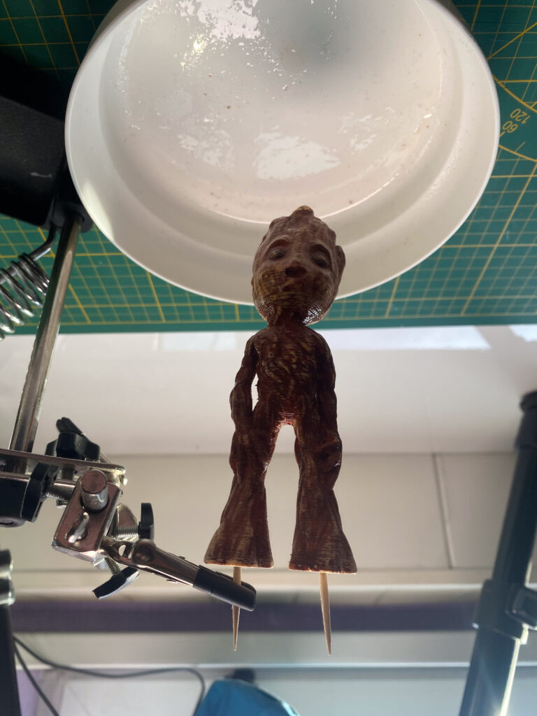 Baby-Groot-Figur in einer Halteklemme unter einer Arbeitsleuchte von unten betrachtet