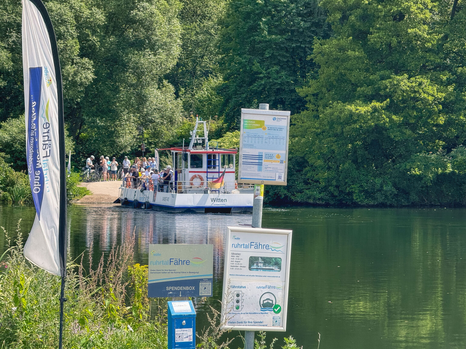 Kleine Personenfähre über die Ruhr mit wartenden Radfahrern am bewaldeten Ufer