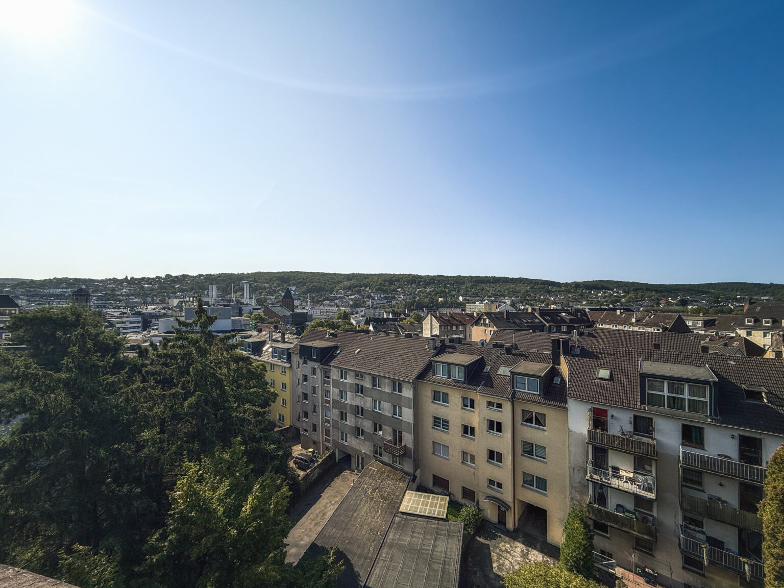 Panorama über eine Stadt im Tal mit bewaldeten Höhen und Wohnhäusern im Vordergrund