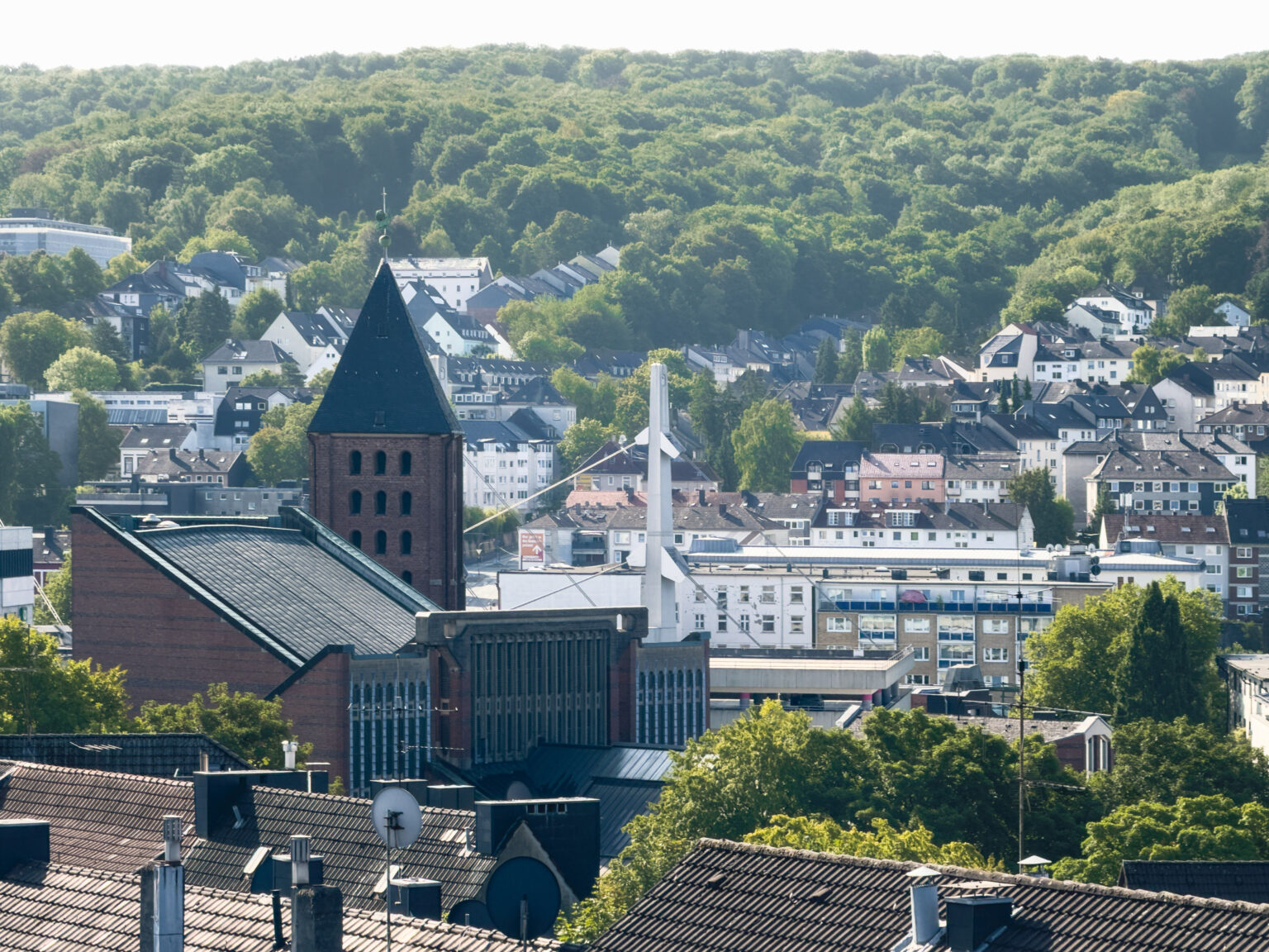 Backsteinkirchturm über der Stadtbebauung im Tal vor bewaldeten Höhenzügen