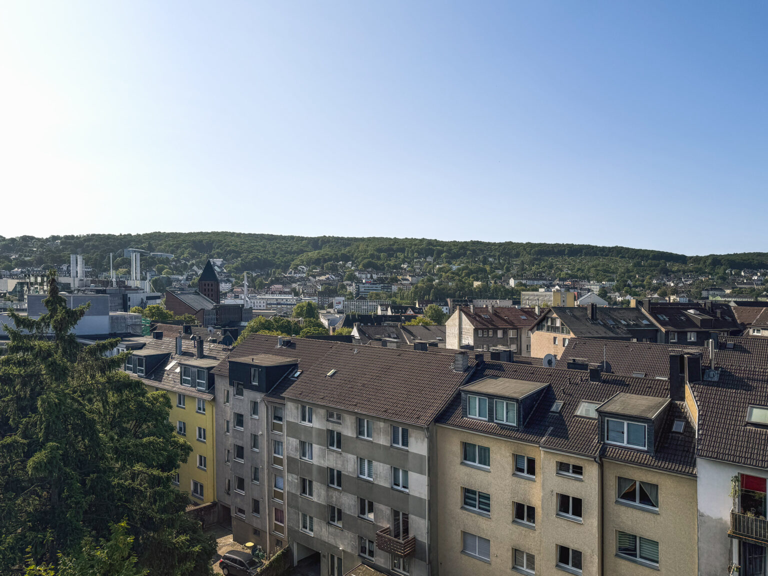 Panorama über Dächer und Wohnblocks einer Stadt im Tal vor bewaldeten Höhenzügen