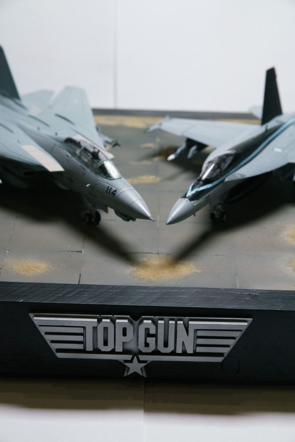 Hochformatige Nahaufnahme zweier Kampfjet-Modelle Nase an Nase über dem Top-Gun-Logo