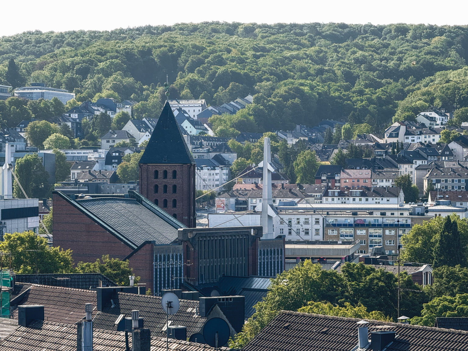 Backsteinkirche mit dunklem Turm vor der Stadt und bewaldeten Höhen