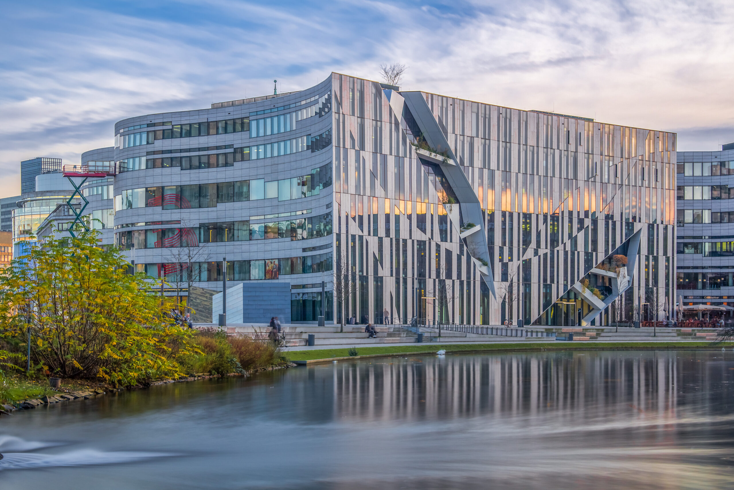 Libeskind's Kö-Bogen reflected in still water in the evening, autumn leaves in front