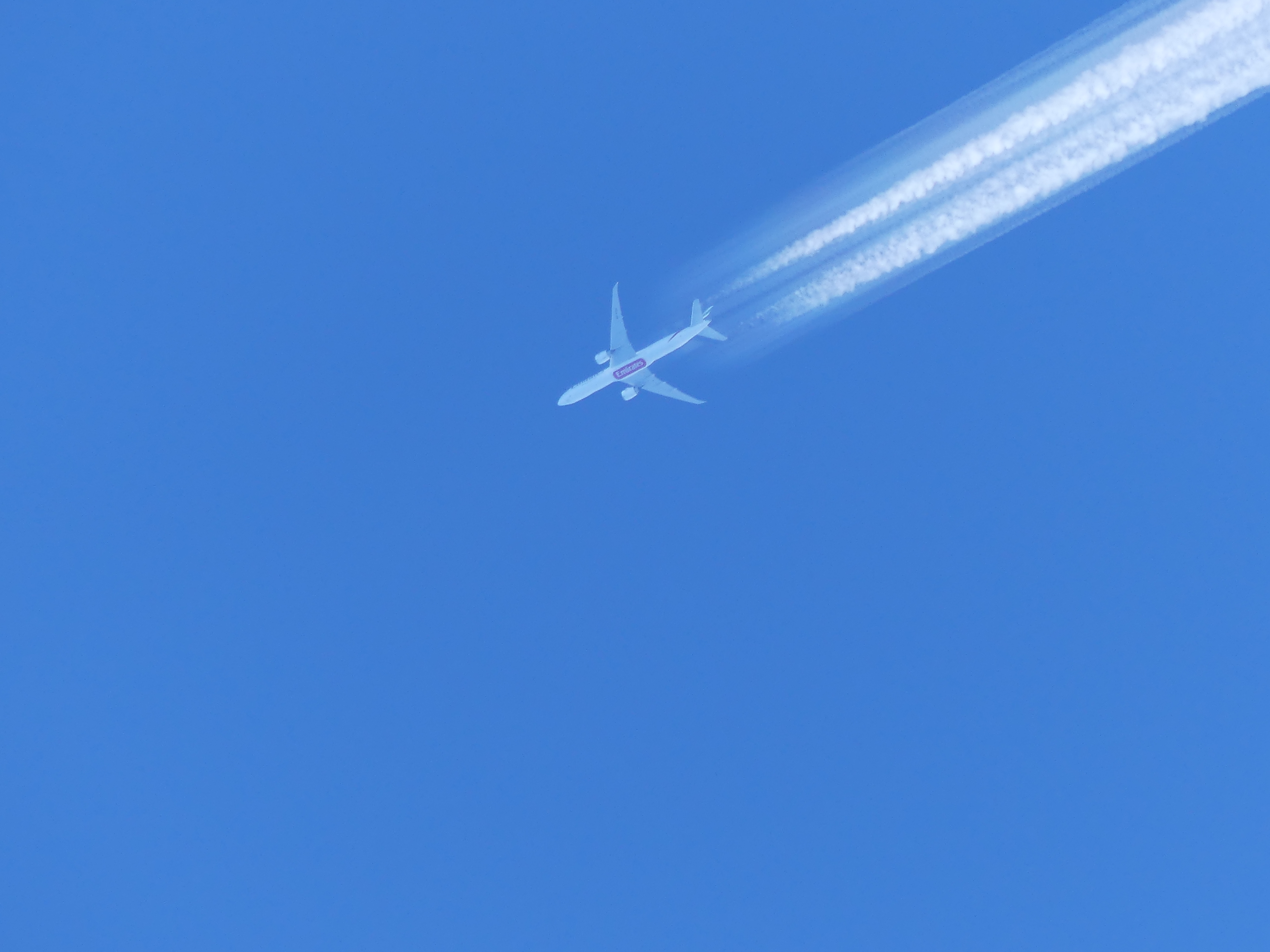 A persistent contrail behind an airliner against a blue sky