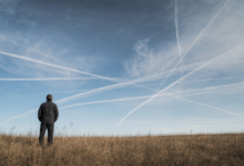 Person blickt in einen Himmel voller kreuzender Kondensstreifen