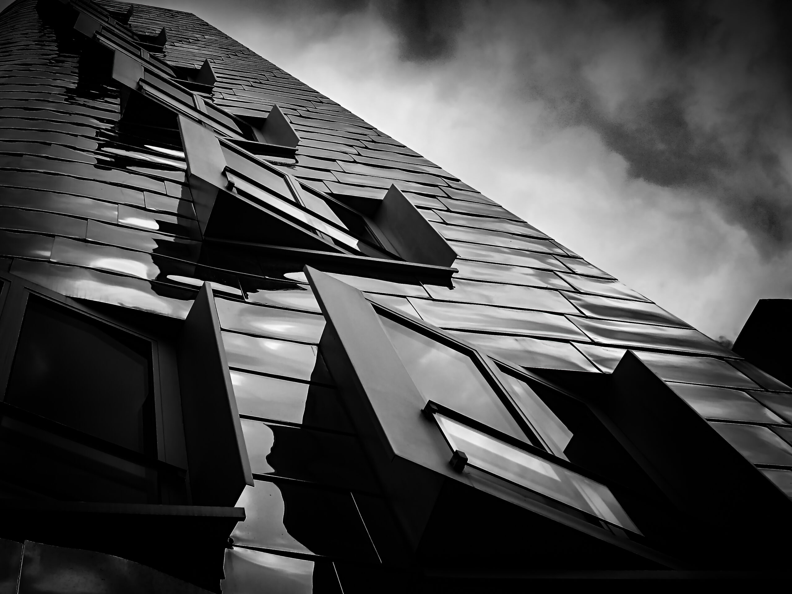 Black-and-white shot of the wavy Gehry facade with protruding windows under a dramatic sky